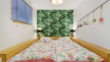 A bedroom with a bed, a window with blinds, a wall tapestry, and a string of cards.