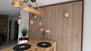 A wooden dining table with a black circular object on top, a hanging light fixture made of wood, and a wall-mounted light.