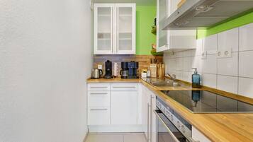 A compact kitchen with white cabinets, a wooden countertop, a built-in oven, and a stainless steel sink.