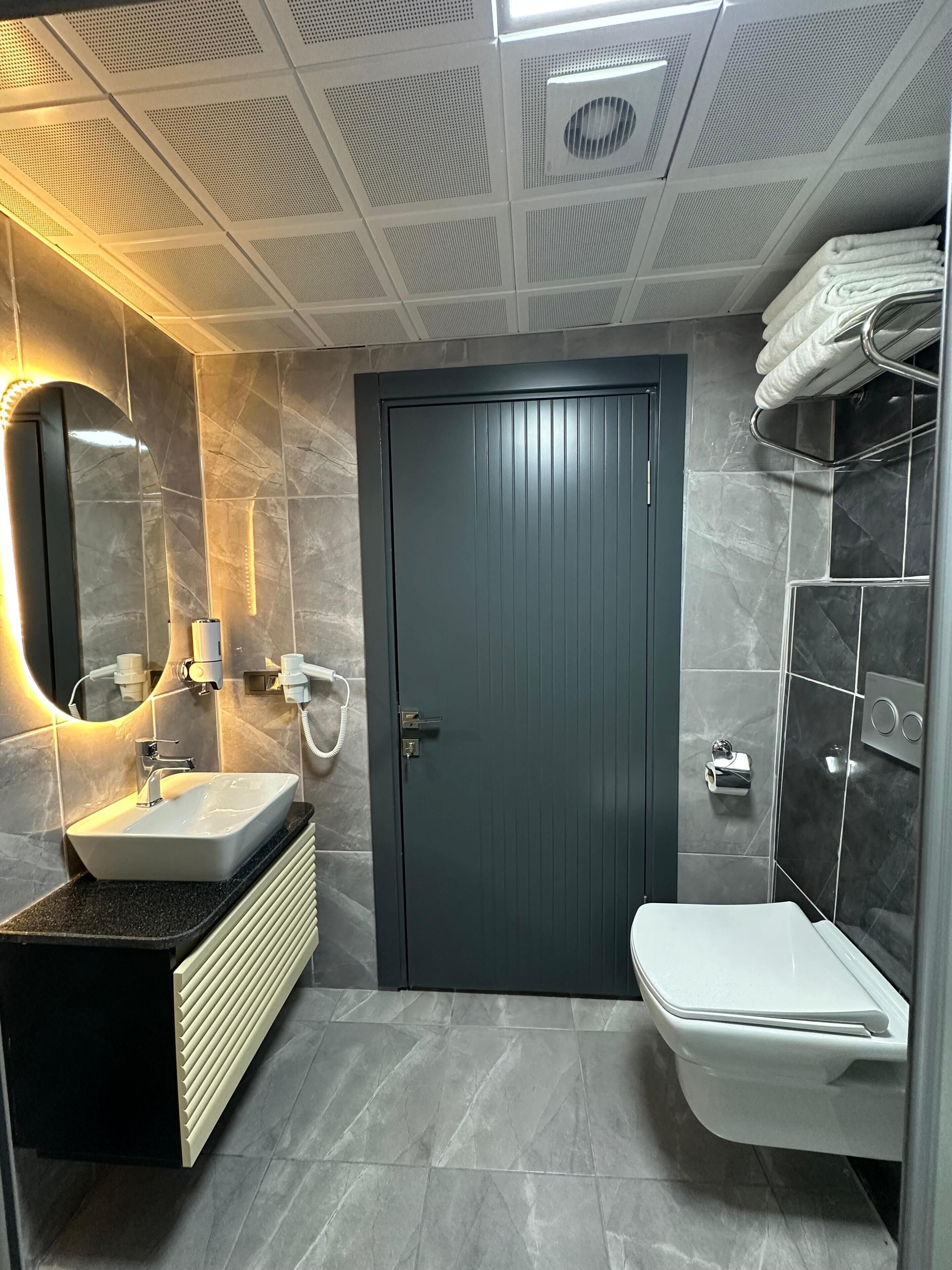 Une salle de bain moderne avec une porte sombre, un lavabo blanc, un miroir, un porte-serviettes et un espace douche.