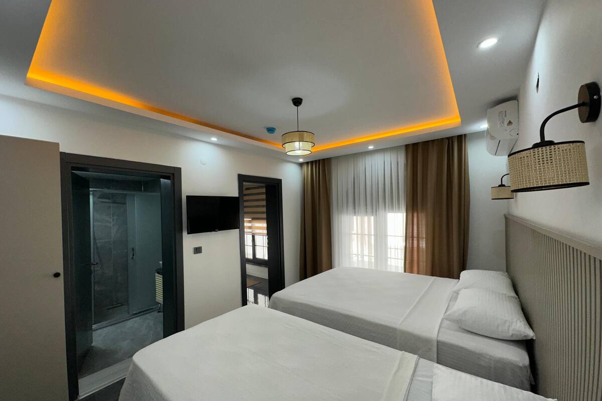 A hotel room with two beds, a TV, a ceiling light, a window with curtains, and a door leading to a bathroom.