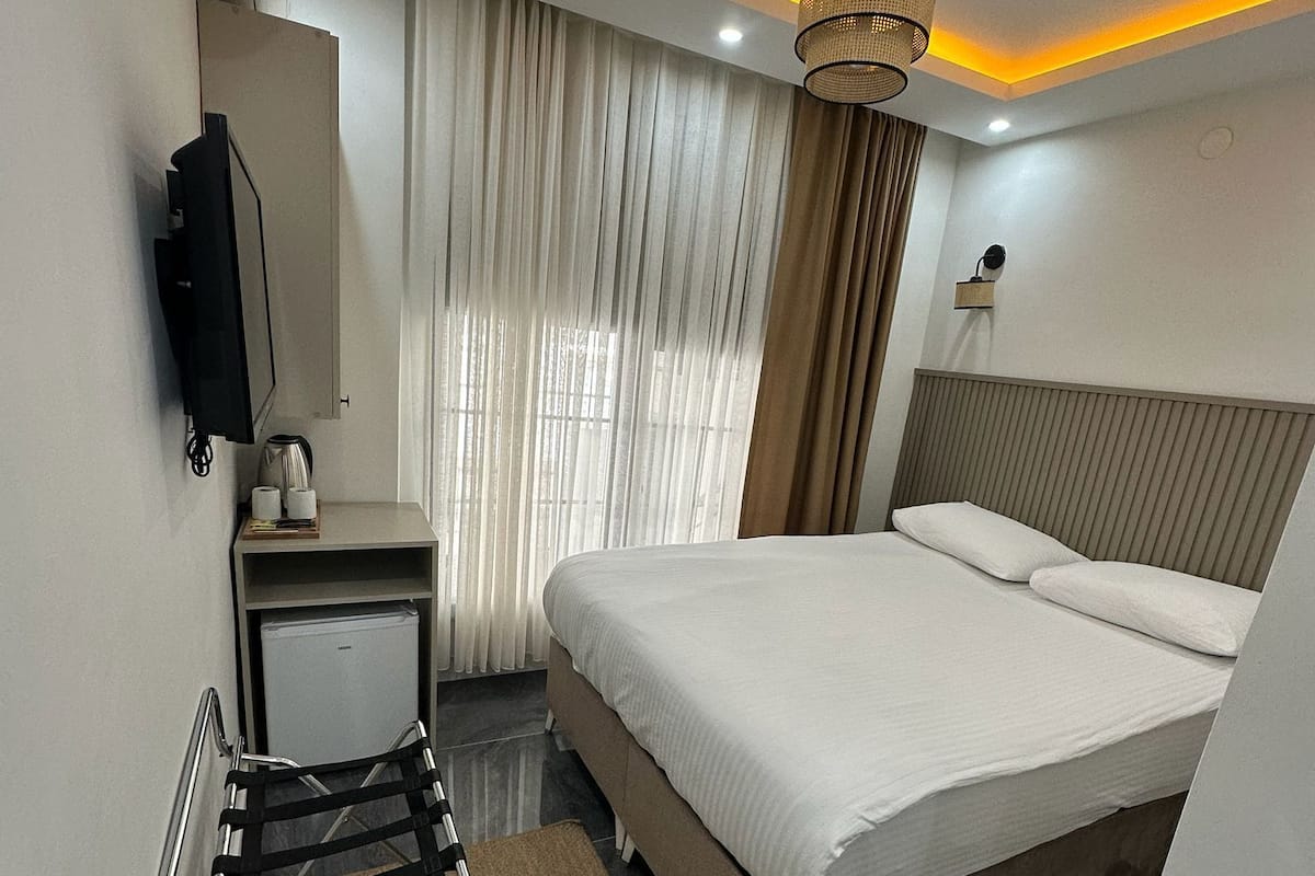 A hotel room with a bed, a desk, a chair, a TV, and a bathroom.