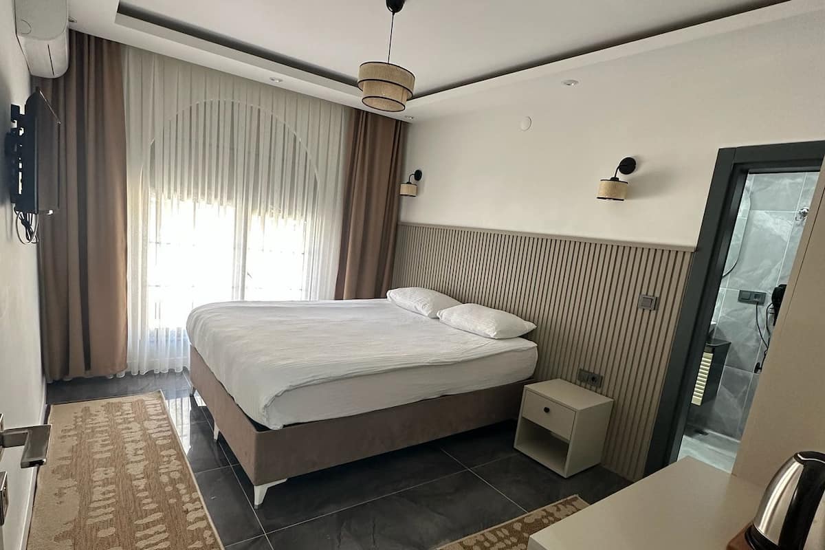 A modern hotel room with a large bed, bedside tables, a small desk, and a mirror.