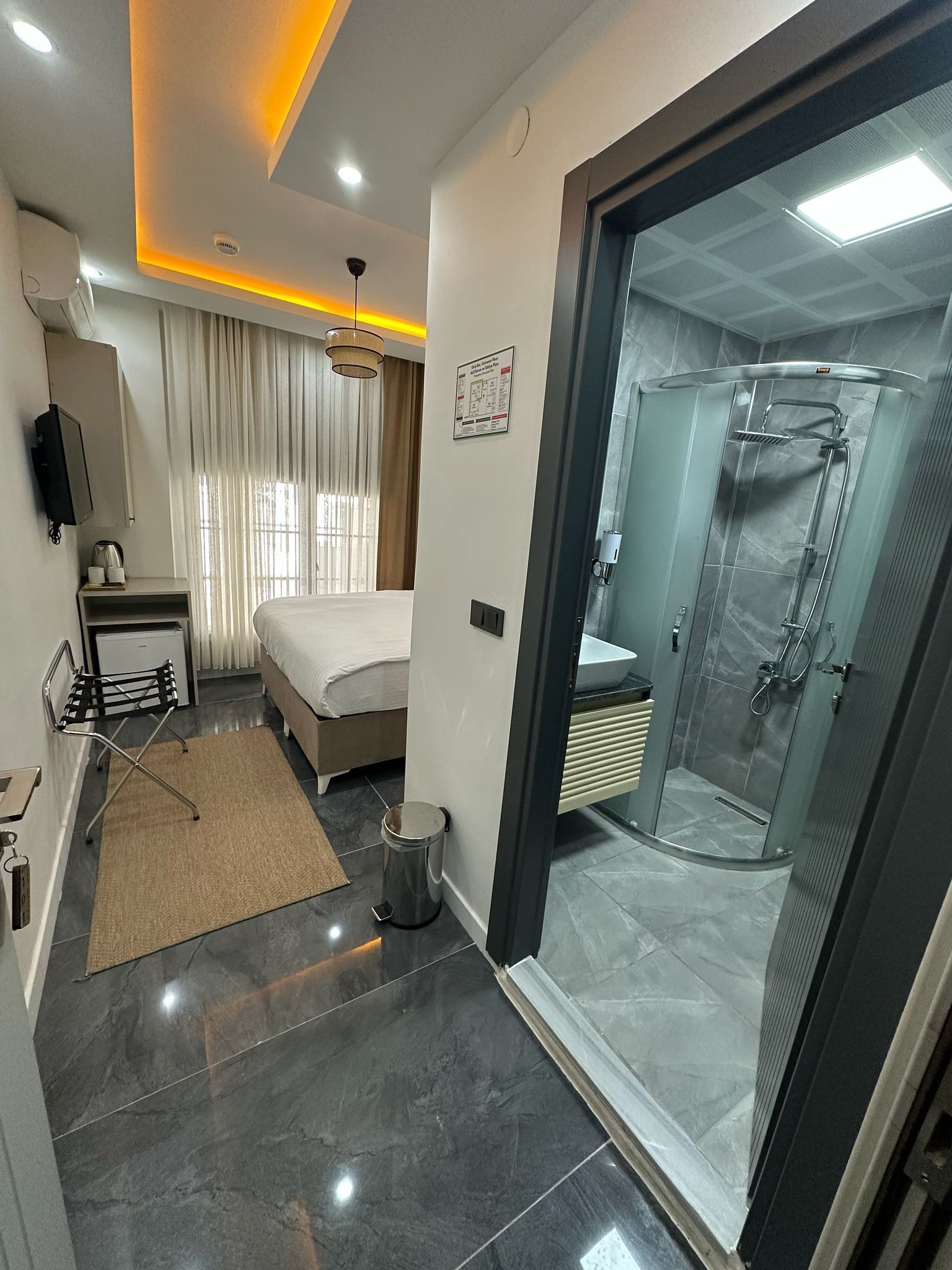A modern hotel room with a bed, bedside table, lamp, and a glass-enclosed shower area.