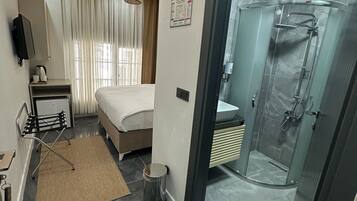 A modern hotel room with a bed, bedside table, lamp, and a glass-enclosed shower area.