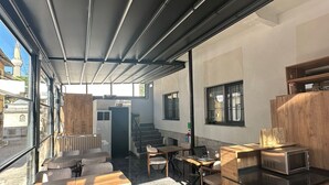 A modern indoor seating area with tables and chairs, a counter with a microwave, and a wet floor sign. - Ay-Asia Suit (Amasya)