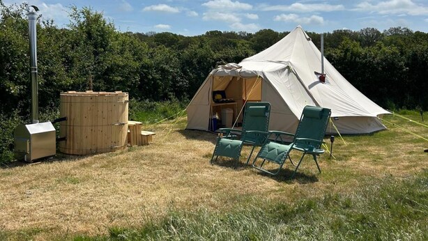 A tent with a chimney, a portable stove, and two green chairs. - Daisys Meadow Retreat Tent Sleeps 2 With Hot Tub (Ashford)