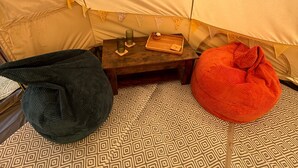 A tent interior with a patterned floor, a small table with a tray, and two bean bags. - Daisys Meadow Retreat Tent Sleeps 2 With Hot Tub (Ashford)