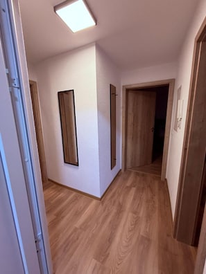 Ein Flur mit Holzdielen, weißen Wänden und einer Deckenleuchte.