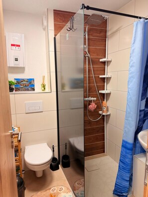 A bathroom with a glass shower enclosure, a toilet, a sink, a showerhead, a shower curtain, and a wall-mounted air conditioning unit.