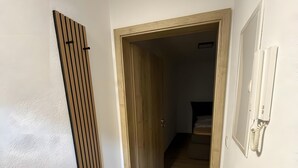 A hallway with a wooden door, a white wall, and a wooden floor.