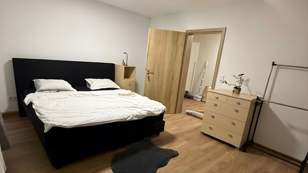 A bedroom with a bed, a dresser, a mirror, and a wooden floor.