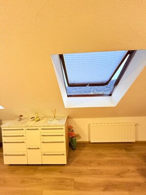 A room with a skylight, a white dresser, and a radiator.