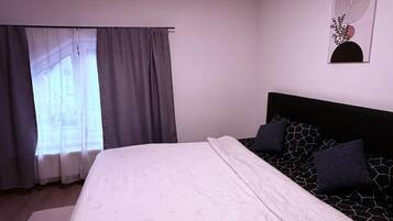 A bedroom with a bed, a window with curtains, a headboard, and a wall-mounted artwork.