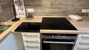 A modern kitchen with a black induction cooktop, a built-in oven, white cabinetry, and a wooden backsplash.