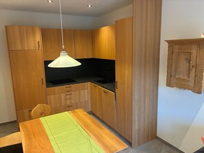Une cuisine moderne avec des meubles en bois, un plan de travail noir, un luminaire suspendu et une table à manger agrémentée d’un set de table vert.