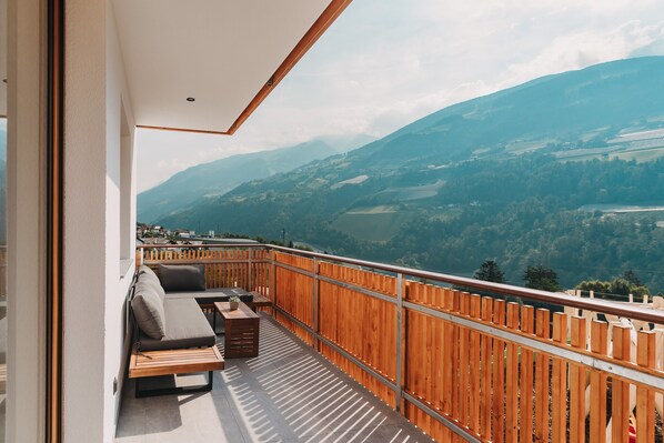 A balcony with a wooden railing, a sofa, and a small table with a plant. - Apartment 'Bergluft Innersennerhof' with Mountain View, Wi-Fi and Air Conditioning (Riffian)