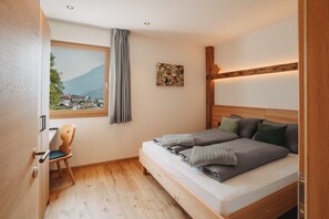 A bedroom with a bed, a chair, a window with a view of houses and mountains, and a painting on the wall. - Apartment 'Bergluft Innersennerhof' with Mountain View, Wi-Fi and Air Conditioning (Riffian)