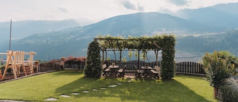 A garden with a wooden pergola covered in greenery, surrounded by a brick pathway.