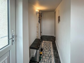 Um corredor com porta, um banco, um tapete e um candeeiro fixado na parede.