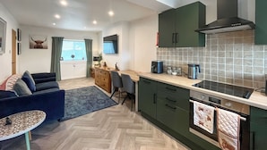 A modern kitchen with green cabinets, a built-in oven, and a herringbone floor pattern.