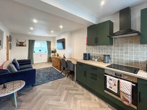 A modern kitchen with green cabinets, a built-in oven, and a herringbone floor pattern.