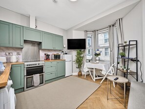 A compact kitchen with a stove, microwave, and a small dining area with a table and chairs. - No.1 Princess Blue Apartments (Portrush)