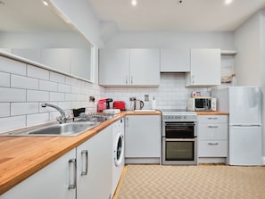 A modern kitchen with white cabinets, a stainless steel sink, a washing machine, a stove, a microwave, and a refrigerator. - No.1 Princess Green Apartments - UK52036 (Portrush)