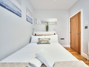 A neatly arranged bedroom with a bed, pillows, a bedside table, a mirror, a wooden door, and a small potted plant. - No.1 Princess Green Apartments - UK52036 (Portrush)