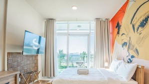 Quarto de hotel com cama, TV fixada na parede, janela com cortinas e vista para o exterior.