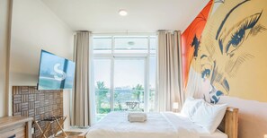 A hotel room with a bed, a TV mounted on the wall, a window with curtains, and a view of the outside. - Resort-Style Studio + Pool & Gym, DAMAC Hills (Dubai)