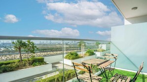 Uma varanda com mesa e cadeiras, guarda-corpo de vidro e vista para a cidade.