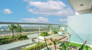 A balcony with a table and chairs, a glass railing, and a view of a cityscape. - Resort-Style Studio + Pool & Gym, DAMAC Hills (Dubai)