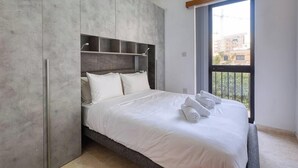 A modern bedroom with a large bed, built-in wardrobe, and a balcony view. - A Premium Apartment in the Heart of Marsaskala (Marsascala MALTA)