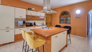 A kitchen with a central island, bar stools, a microwave, and a stove. - A Premium Apartment in the Heart of Marsaskala (Marsascala MALTA)
