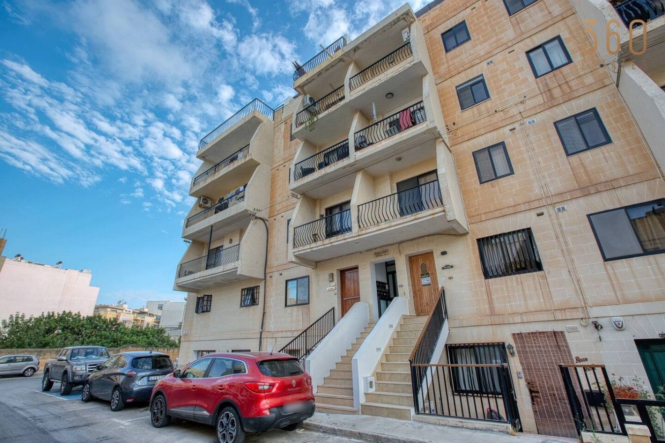 A multi-story residential building with balconies, a staircase, and parked cars.