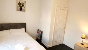 A hotel room with two beds, a white door, a nightstand with a lamp, and a ceiling light. - Cozy Apartment in Barrow-in-furness (Barrow-in-Furness)
