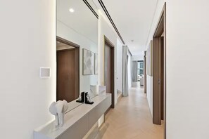 Un pasillo moderno con suelo de tonos claros, una recepción con una escultura blanca, obras de arte enmarcadas y una puerta de madera.