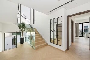 Un interior moderno con una escalera, barandas de vidrio y una gran planta en maceta.