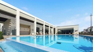 En swimmingpool med solstolar och parasoller, ett överbyggt område och en klarblå himmel.