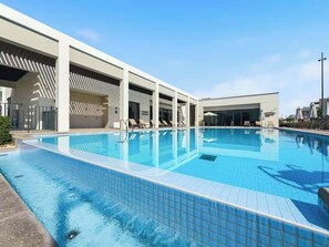 Una piscina con sillas de descanso y sombrillas, un área techada y un cielo azul despejado.