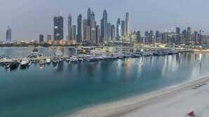 Un port de plaisance avec des bateaux amarrés, une plage de sable et une vue sur les gratte-ciel d’une ville.