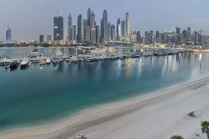 Un port de plaisance avec des bateaux amarrés, une plage de sable et une vue sur les gratte-ciel d’une ville.