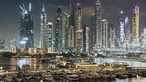 Une vue nocturne d’une ville avec de hauts immeubles et un port de plaisance rempli de bateaux.