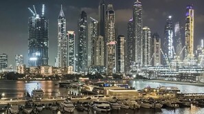 Une vue nocturne d’une ville avec de hauts immeubles et un port de plaisance rempli de bateaux.