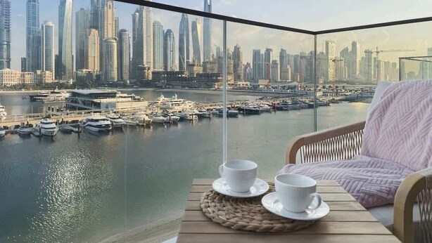Un balcon offrant une vue sur les toits de la ville, une table avec deux tasses blanches et une chaise en osier.