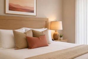Ein ordentlich bezogenes Bett mit Kopfteil, einer Nachttischlampe und einem gerahmten Bild an der Wand.
