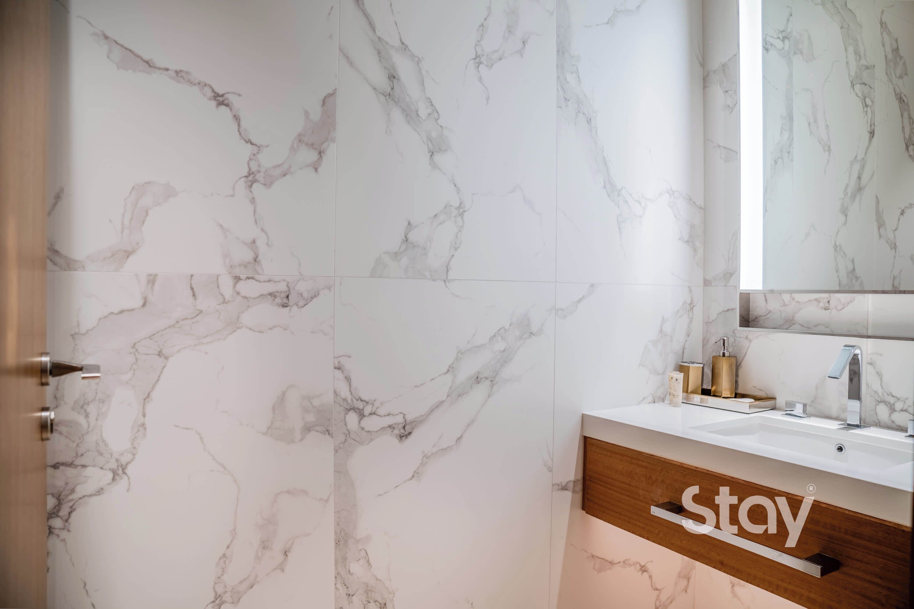 A bathroom with marble walls, a wooden vanity, a sink, and a mirror.