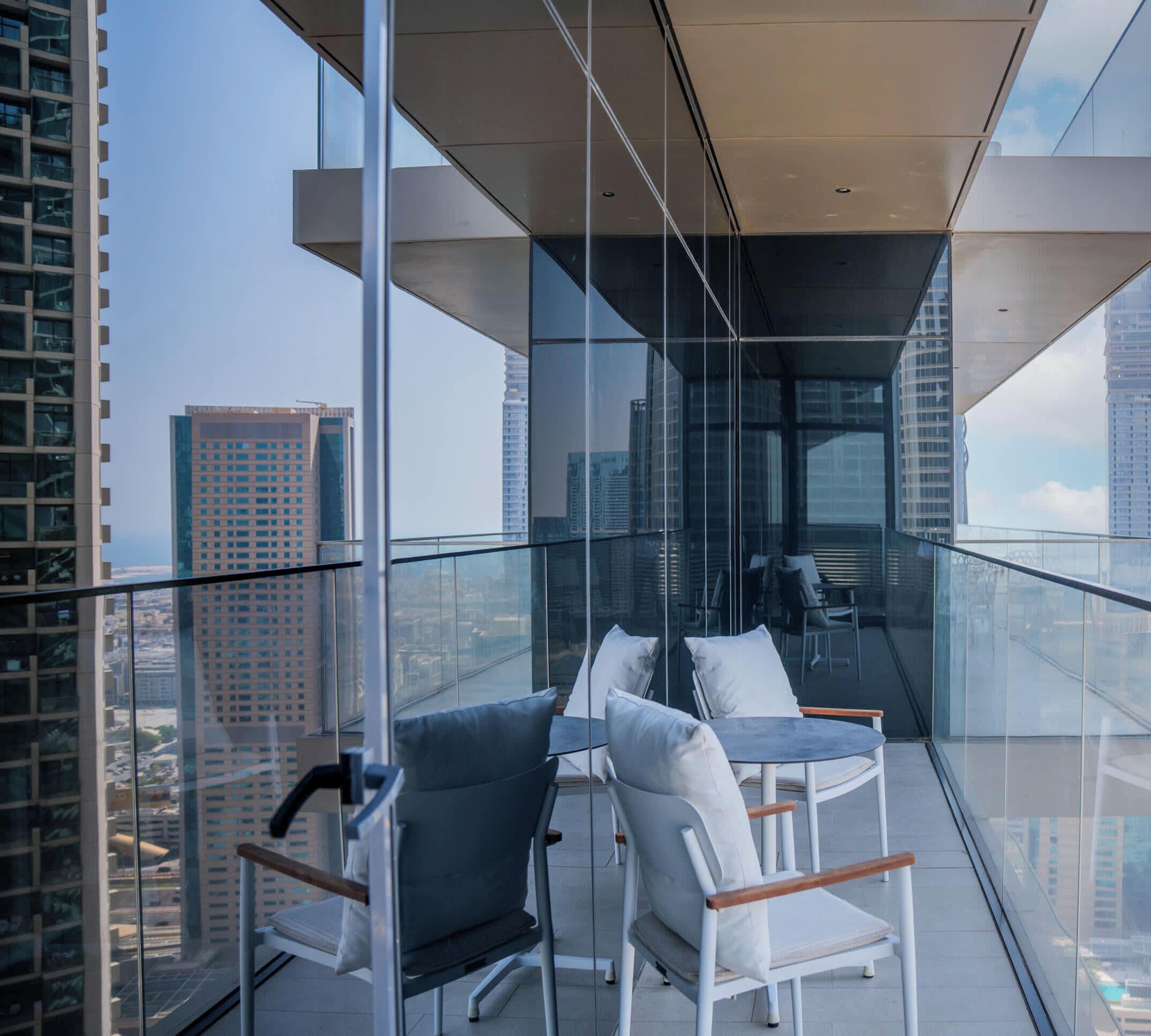 A modern balcony with glass railings, two chairs, and a table.