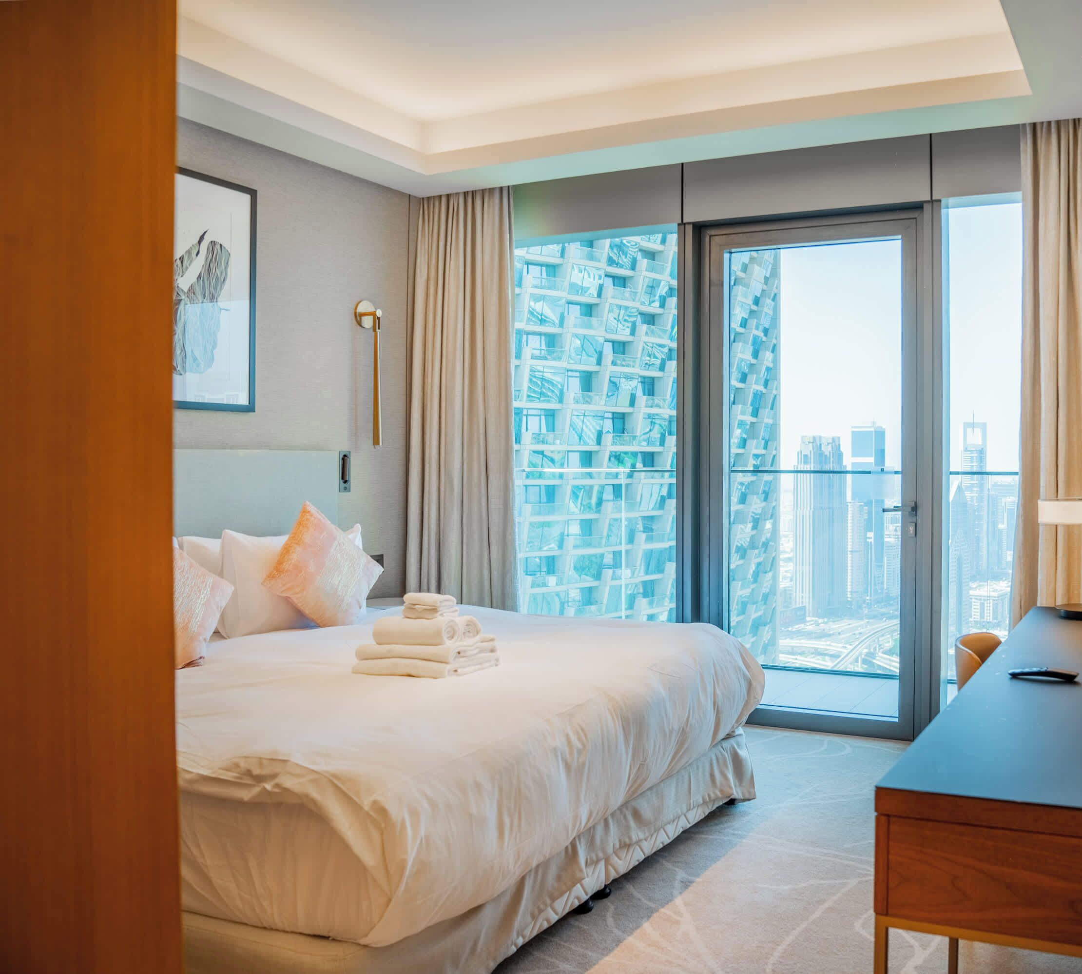 Ein Hotelzimmer mit Bett, Schreibtisch und Blick auf eine Stadtlandschaft, sowie einem großen Fenster.